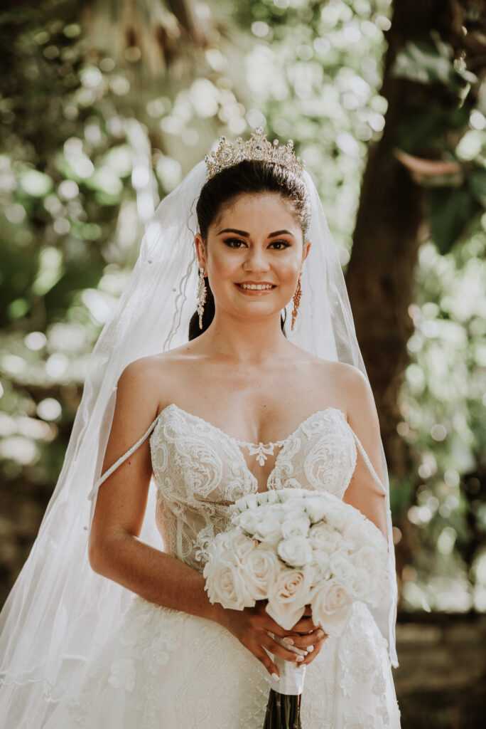 Novia vestida de blanco con ramo de rosas blancas en las manos. Foto sonriendo a la cámara. Boda en La Habana, Cuba.