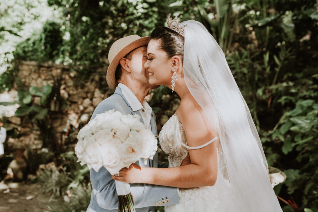 Novia vestida de blanco besa a su papá antes de la boda. Novia con ramo de rosas blancas en la mano y vestida de novia con su papá antes de la ceremonia. Boda en La Habana, Cuba