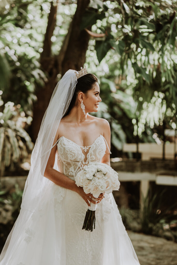 Novia vestida de blanco, con ramo de rosas en sus manos. Foto de novia sonriendo de perfil. Boda en La Habana, Cuba.