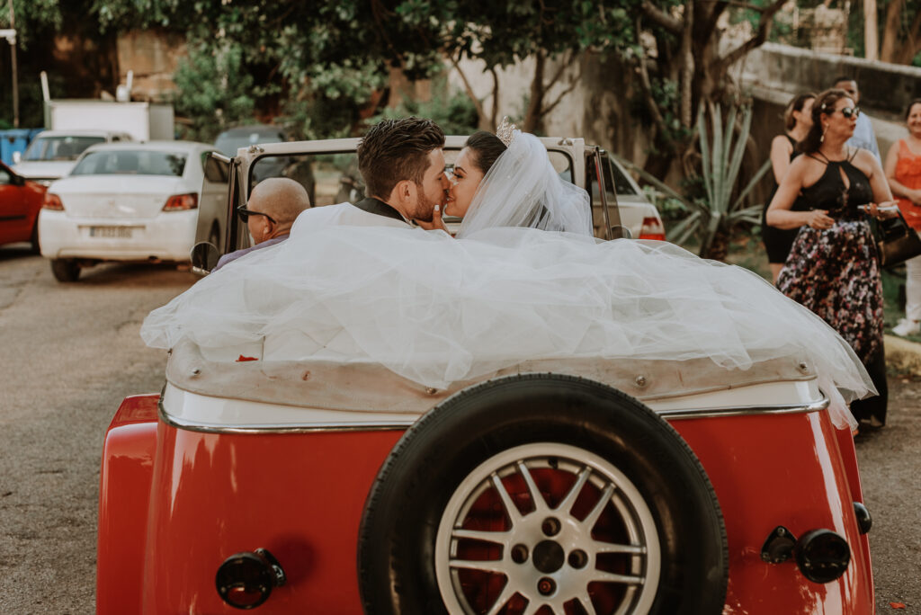 Novios pasean en auto antiguo descapotable, blanco y rojo, por La Habana.