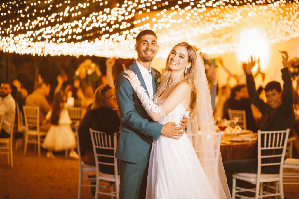 Pareja de recién casados delante de su cena de bodas en jardín con fairylights